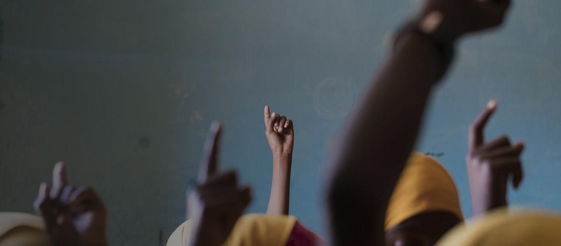 Close up photo of the tops of girls heads with one finger raised high in the air. 