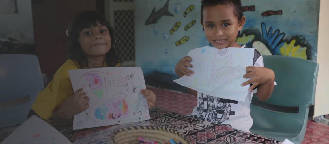 Two small children proudly hold up their drawings.