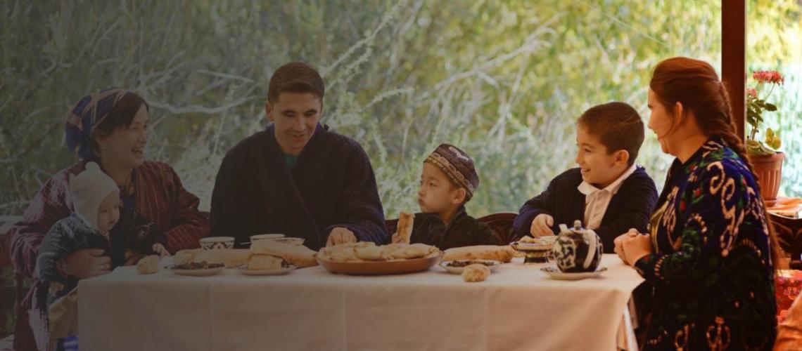 An Uzbek family sits happily together at a dining table having lunch.
