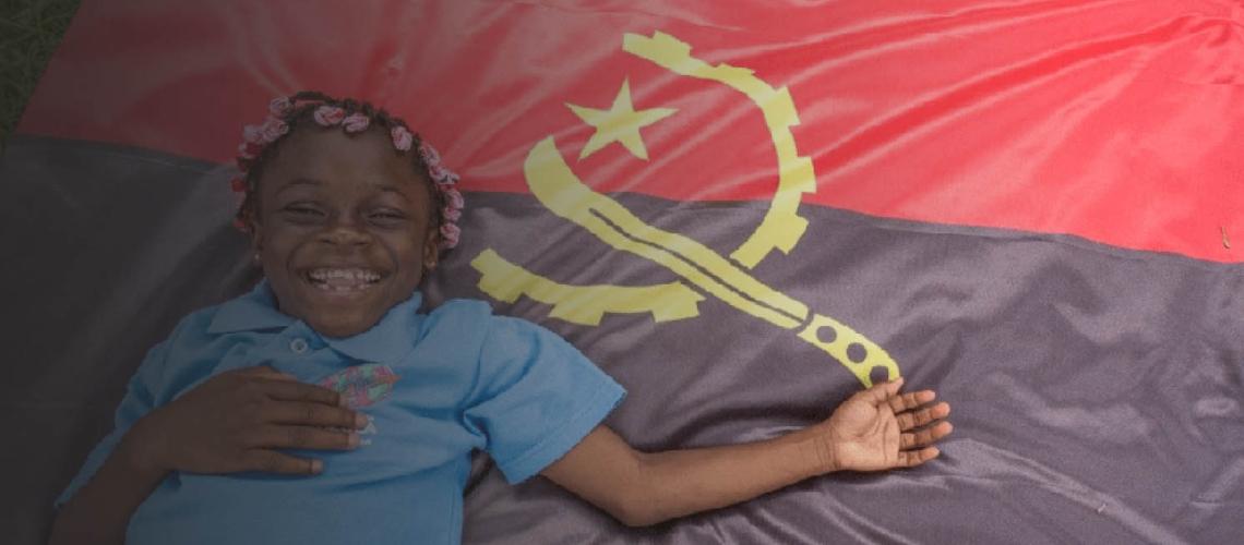 A little girl happily smiles as she lays upon the Angola flag.