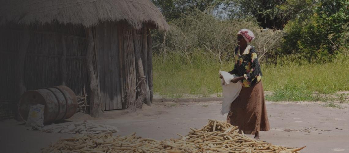 A woman smiles as she is outside a home as she stands above a pile of corn.