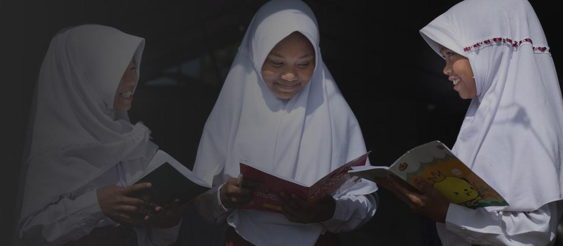 تبتسم ثلاث فتيات من مدرسة ابتدائية بينما يقرأن كتبهن.