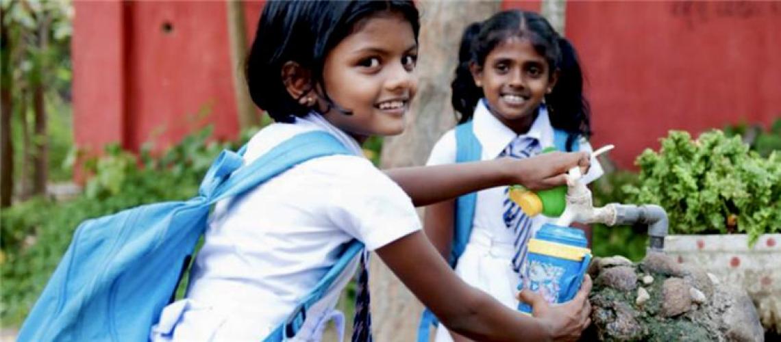 Two girls with blue back packs on their backs smile at the camera.
