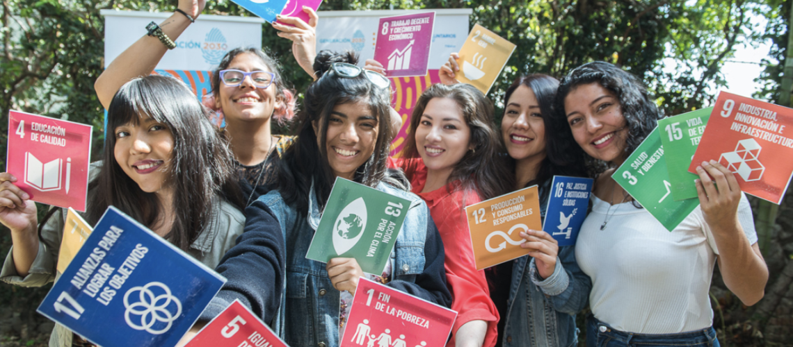 A group of young people hold up the multi-colored Sustainable Development Goals.