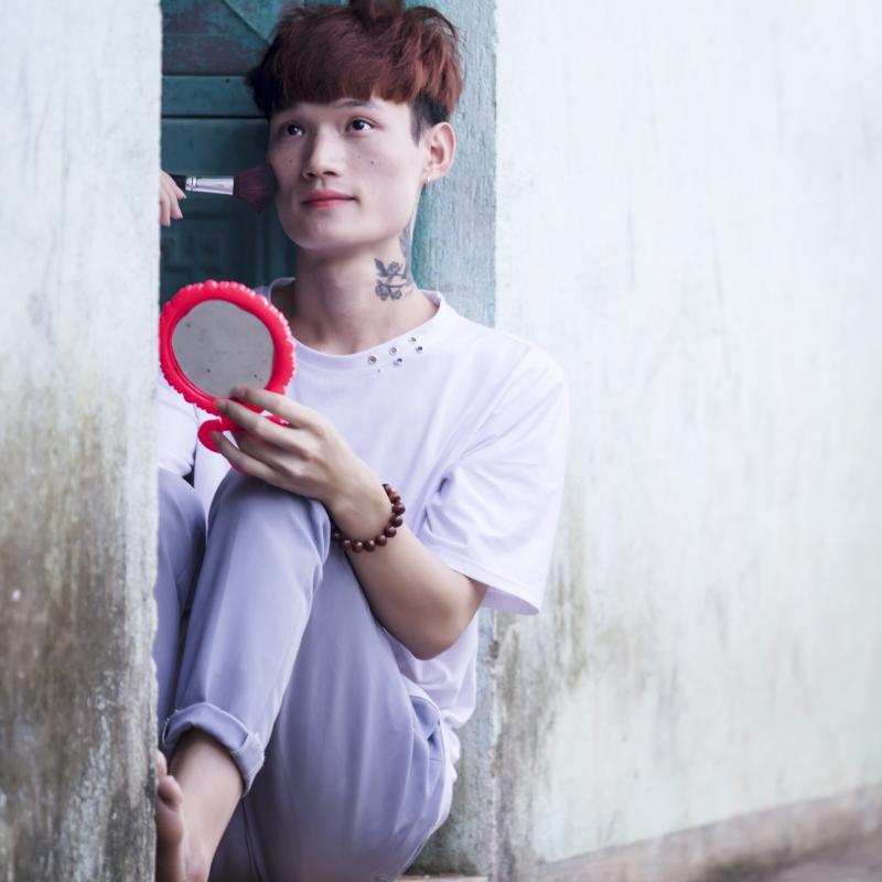 Bui Thi Chi sits crouched in a doorway as she applies makeup.